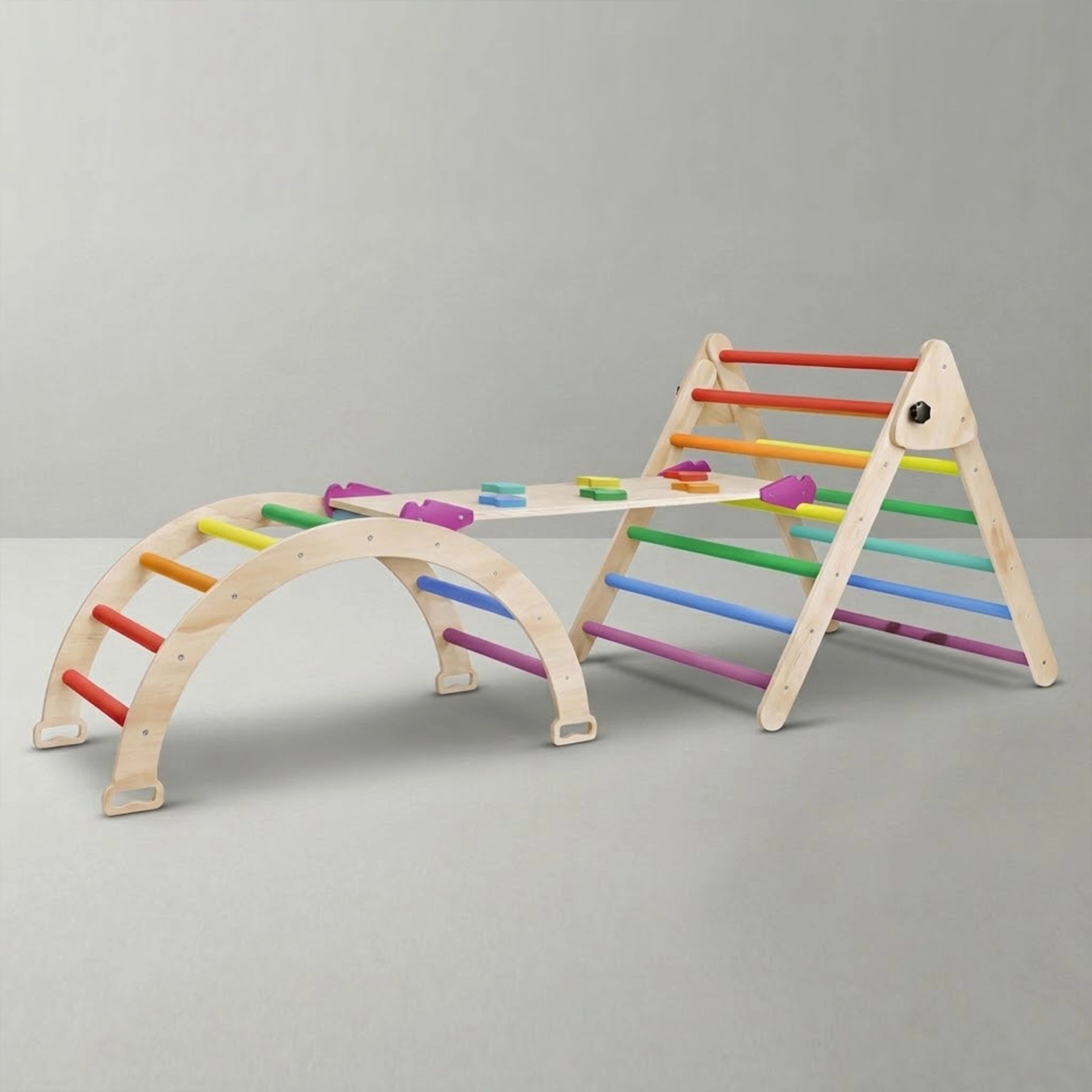 A clean studio shot of a 3-piece children's wooden Montessori climbing set against a light grey background. It clearly displays the climbing arch on the left and the Pikler triangle on the right, both with bright rainbow rungs, seamlessly connected by a wooden rock climbing ramp.