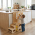 Toddler boy interacting with the yellow safety knobs on an adjustable Hicooo wooden learning tower in a modern kitchen setting