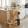 Toddler boy interacting with the yellow safety knobs on an adjustable Hicooo wooden learning tower in a modern kitchen setting