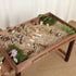  Elevated wooden sandbox for kids filled with sand and miniature city toys including wooden cars, road signs, houses and trees for imaginative outdoor play