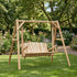 A lifestyle photograph capturing a freestanding rustic wooden log A-frame swing set with a stand, placed on a grassy lawn next to a brown wooden house and a patio in a sunny garden backyard.