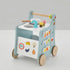 A side perspective studio shot of a freestanding wooden 6-in-1 toddler activity walker and play kitchen. Shows the side with the movable food slider, gear-driven clock, shape sorting puzzle, and prominent natural wood grain. For ages 12+ months.