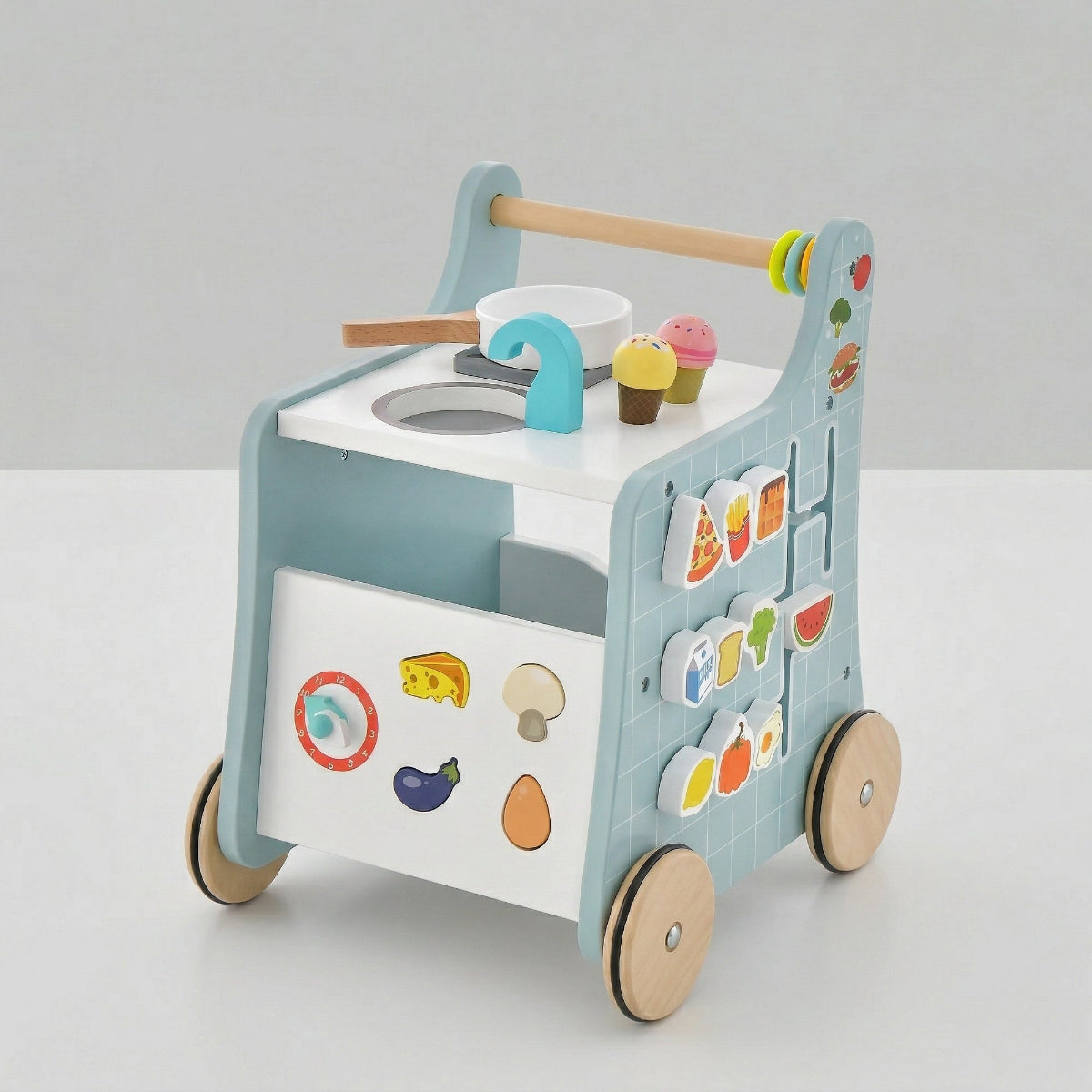 A side perspective studio shot of a freestanding wooden 6-in-1 toddler activity walker and play kitchen. Shows the side with the movable food slider, gear-driven clock, shape sorting puzzle, and prominent natural wood grain. For ages 12+ months.