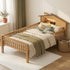 A full-length lifestyle photograph of a complete house-shaped wooden twin bed frame for children. It stands on a soft beige rug in a tidy playroom. The bed is made of natural wood and white painted components, showing the full slat base. A small plush animal toy sits on the bed, and a toy basket is visible in the background against a neutral wall. A small child's hand subtly touches the lower frame.