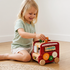 A smiling little girl sitting on a rug, successfully placing a tiger block into the shape sorter of the HiCOOO wooden animal bus.