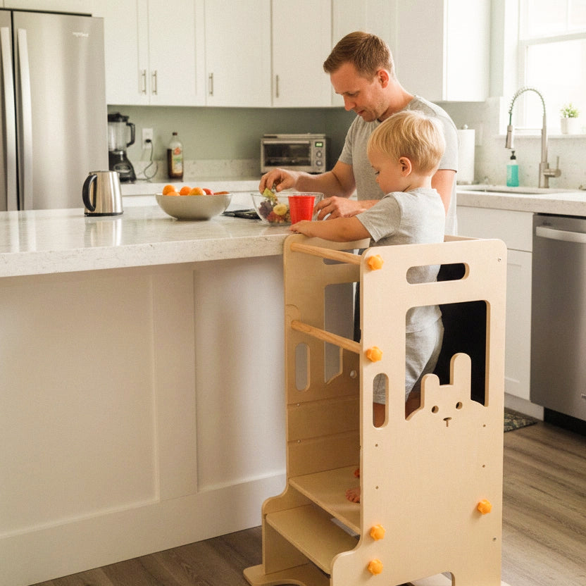 A young toddler in pajamas independently climbing up the built-in step of the HICOOO wooden learning tower. Demonstrates easy access and Montessori-style independence in the kitchen.