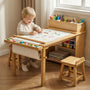 Lifestyle shot of a happy toddler boy sitting on a stool, drawing with crayons on the Hicooo wooden art table. He is using the large paper roll, with markers and supplies neatly stored in the top organizer and side shelves.