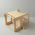 A side angle view of the Hicooo natural wood toddler tower converted into a small play desk and bench seat, resting on a light grey surface.