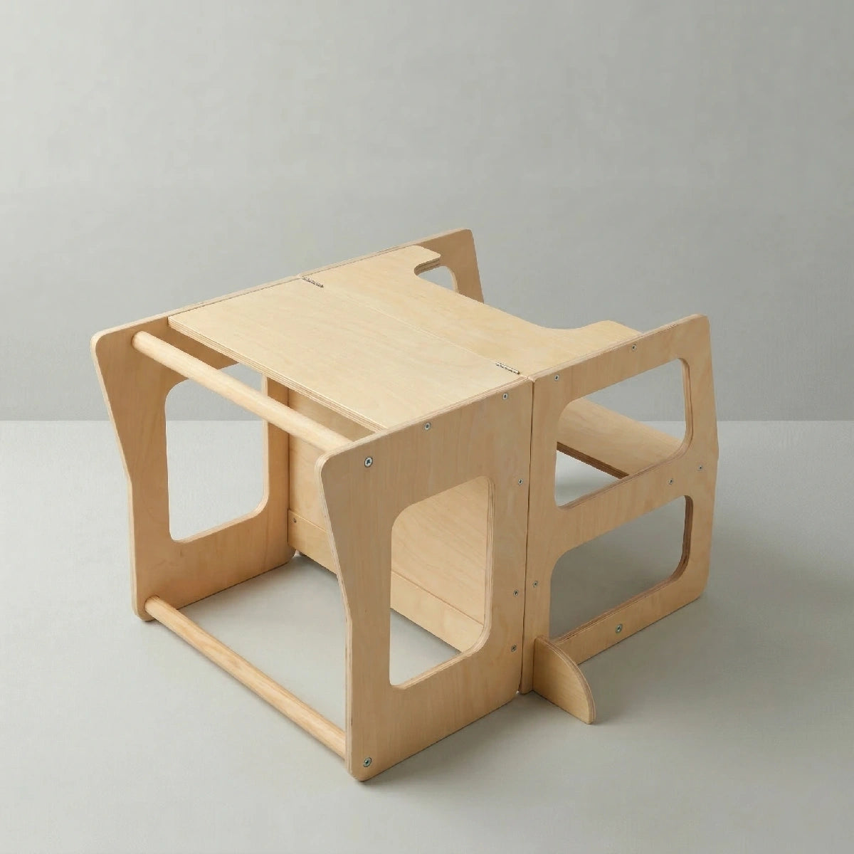 A side angle view of the Hicooo natural wood toddler tower converted into a small play desk and bench seat, resting on a light grey surface.