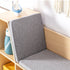 A close-up view of the built-in reading bench on a light wood kids' bookcase, focusing on the comfortable grey fabric cushions for the seat and angled backrest. A blue water bottle is conveniently stored in the adjacent open cubby, highlighting the practical and ergonomic design.