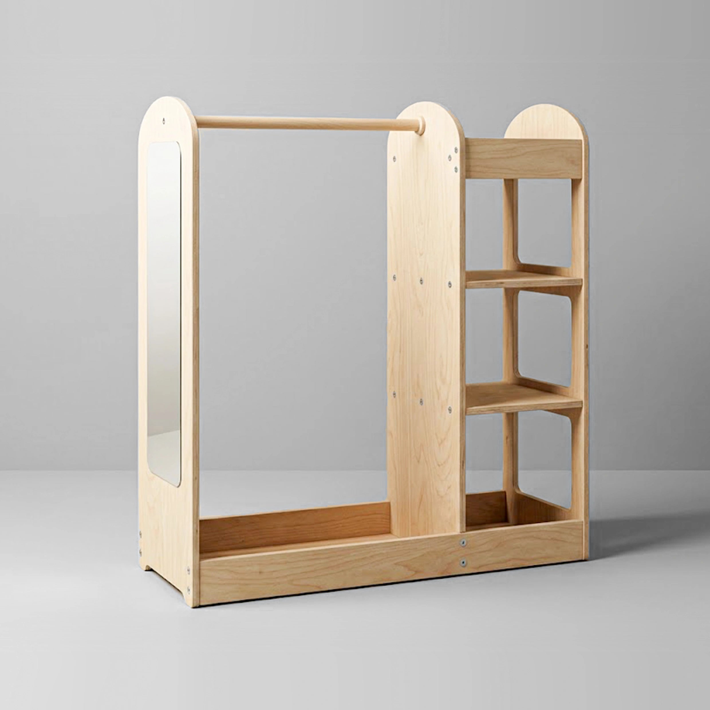 A studio shot of a modern, light wood kids' dress-up center and open wardrobe against a solid grey background. The unit features a solid wood hanging rod, a built-in child-safe mirror on the left side panel, a bottom storage tray, and three open shelves on the right.