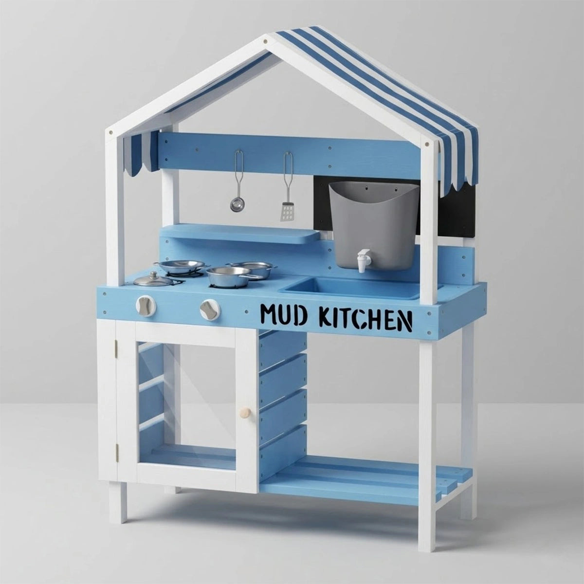 A clean studio photograph of a light blue and white wooden kids mud kitchen against a plain gray background. This angle highlights the empty lower storage section, clearly showing the white cabinet door with a transparent window and the blue slatted shelves underneath. The countertop features the text "MUD KITCHEN", two stove knobs, a sink basin, and a pretend stovetop with stainless steel toy pots. The upper panel includes a striped awning, a grey water tank with a spigot, hanging cooking utensils, and a b
