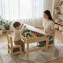 Lifestyle shot of a mother and toddler lifting the reversible top of the Hicooo wooden activity table. Reveals the deep hidden storage compartments inside, filled with children's books and wooden toys.