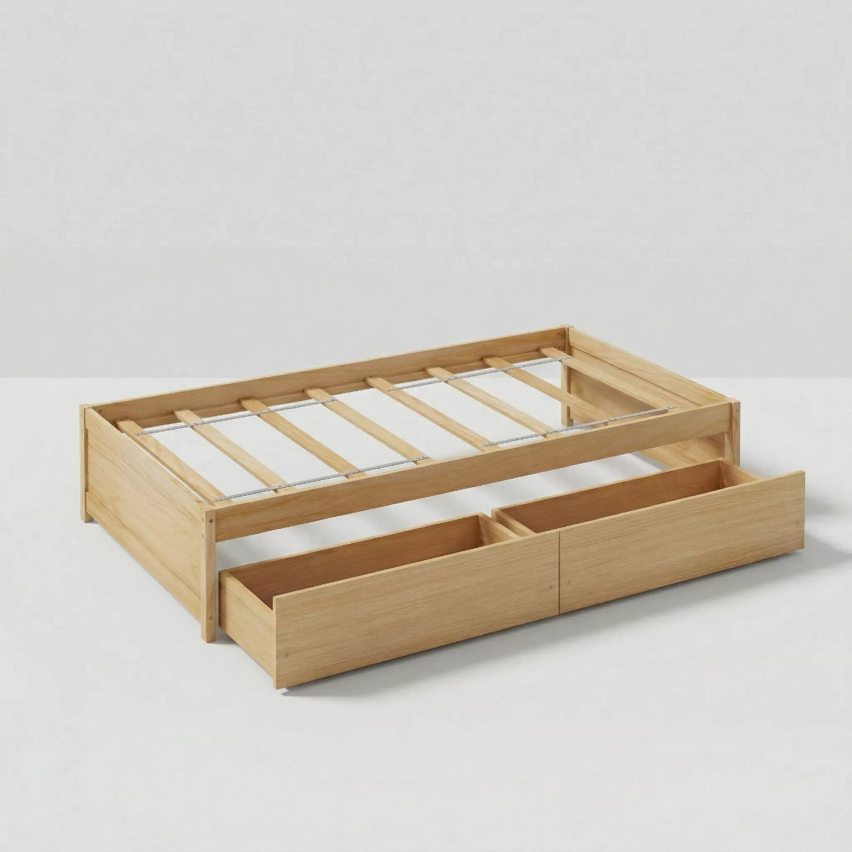 A studio photograph on a white background, featuring a clean, white-painted wooden twin-size platform bed frame. It displays a slat support system, a low headboard with simple vertical planks, a matching footboard, and two built-in pull-out storage drawers on wheels.