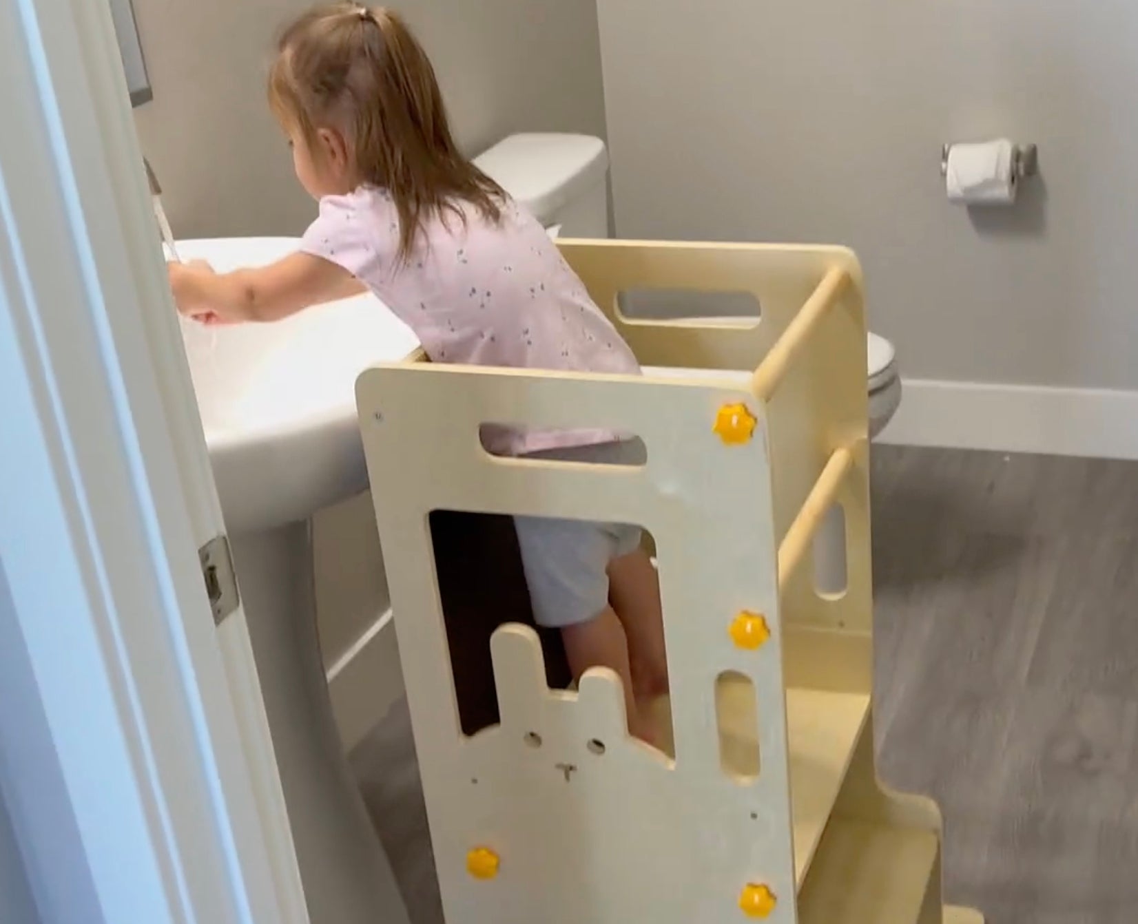 Side view of a child using a sturdy wooden helper tower to reach the faucet, demonstrating the product's versatility for bathroom hygiene routines."