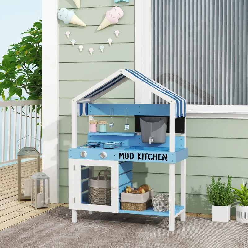 A studio shot of a wooden kids mud kitchen painted in light blue and white, featuring a charming striped canopy roof. The play set includes a pretend stovetop with toy pots, a sink basin, a functional-looking grey water dispenser with a tap, hanging utensils, and a small chalkboard. The text "MUD KITCHEN" is boldly printed on the front counter. The lower section features a white storage cabinet with a clear window door and open shelving holding woven baskets, set against a plain light gray background.
