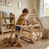 A toddler boy stands and plays with colorful wooden blocks on top of the Hicooo convertible wooden desk in a cozy playroom decorated with a teepee and bookshelf.