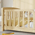 A light natural wood toddler bed with safety vertical slats, styled with a yellow woven blanket and a plush toy in a softly lit room.