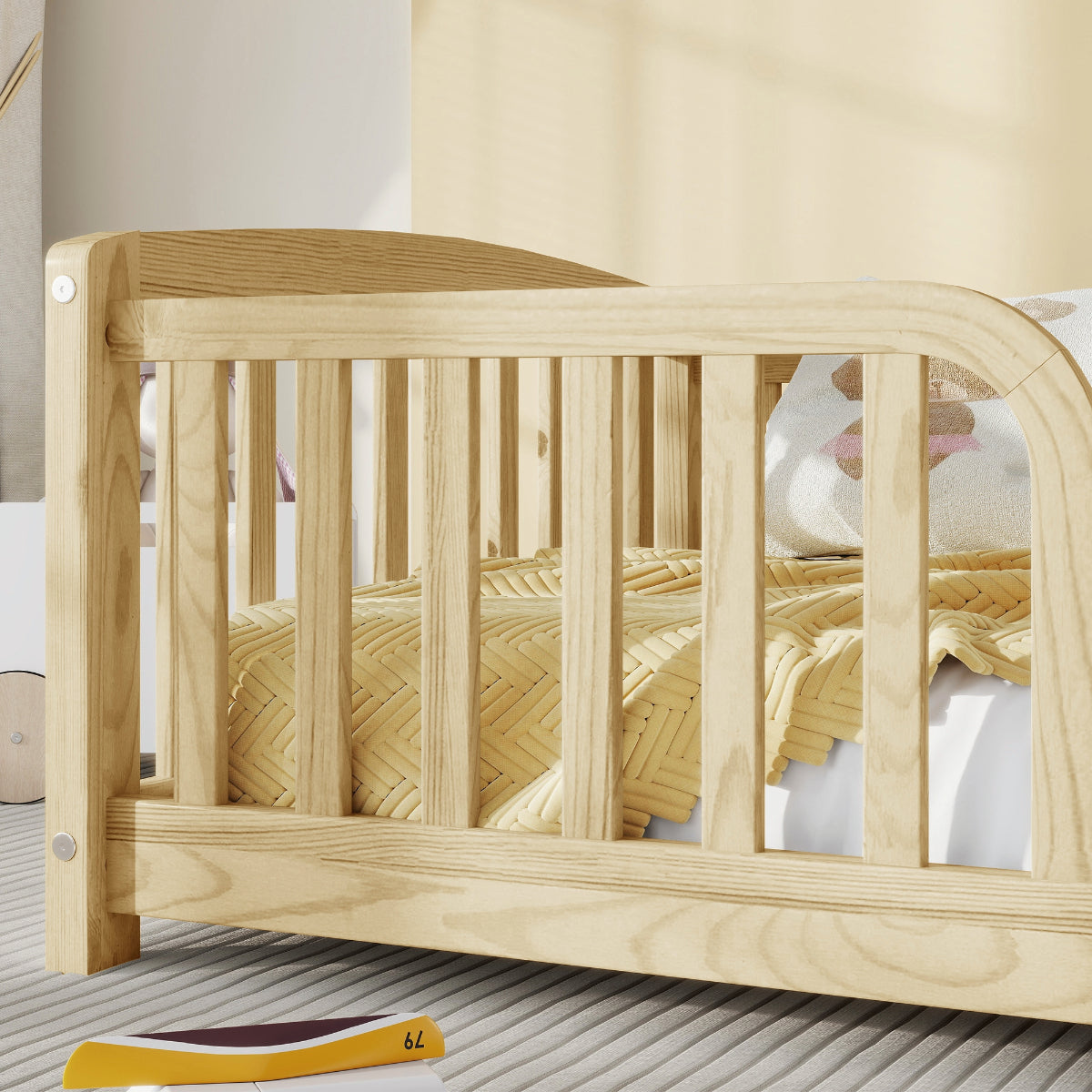 A light natural wood toddler bed with safety vertical slats, styled with a yellow woven blanket and a plush toy in a softly lit room.