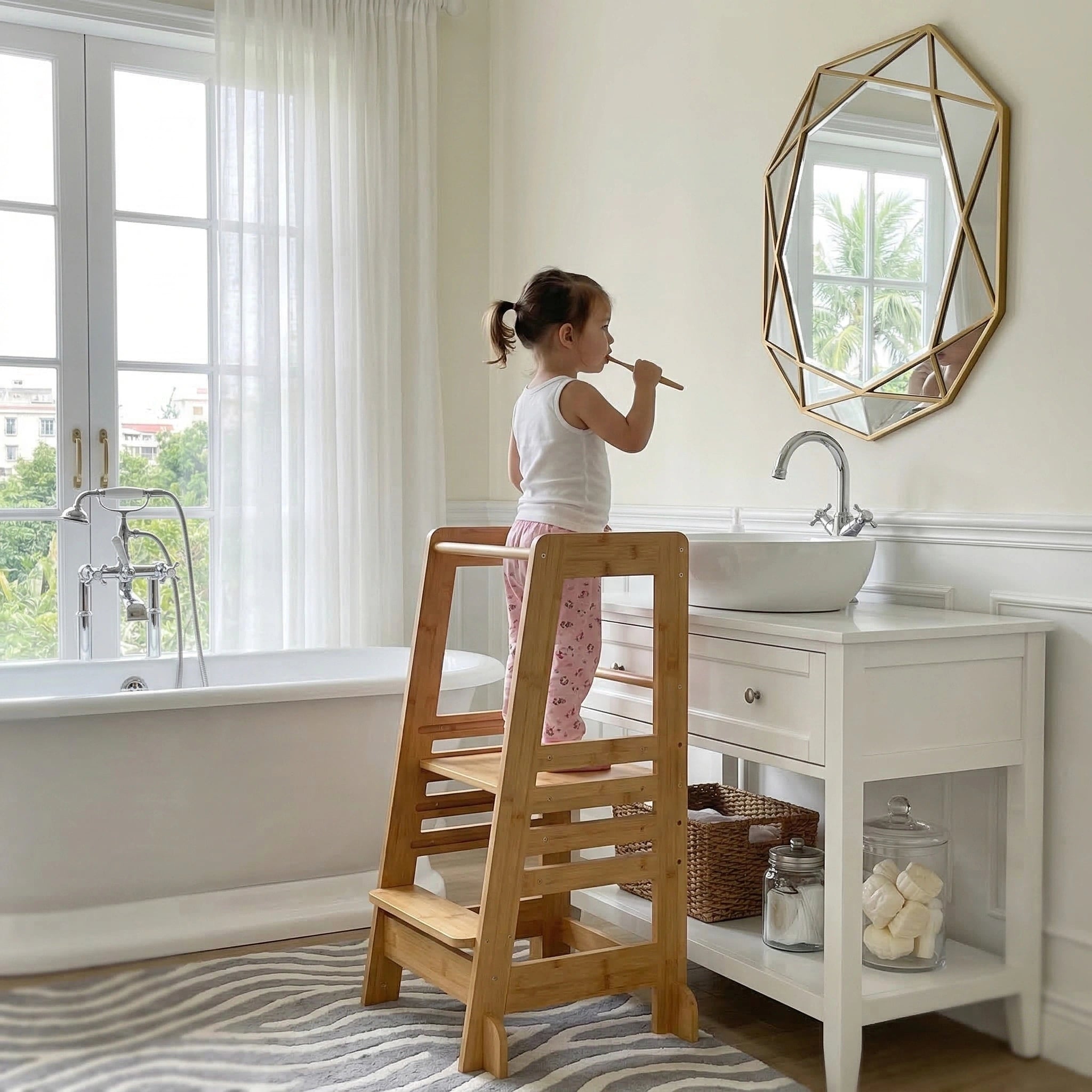 A toddler girl stands independently on the Hicooo natural bamboo step stool in a bright bathroom, brushing her teeth in front of a modern vanity mirror next to a white bathtub.