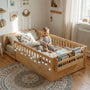 Lifestyle photography of the Hicooo wooden Montessori floor bed. Features safety guardrails, a built-in storage bookshelf at the footboard, and cozy LED string lights, showing a toddler happily playing on the mattress.