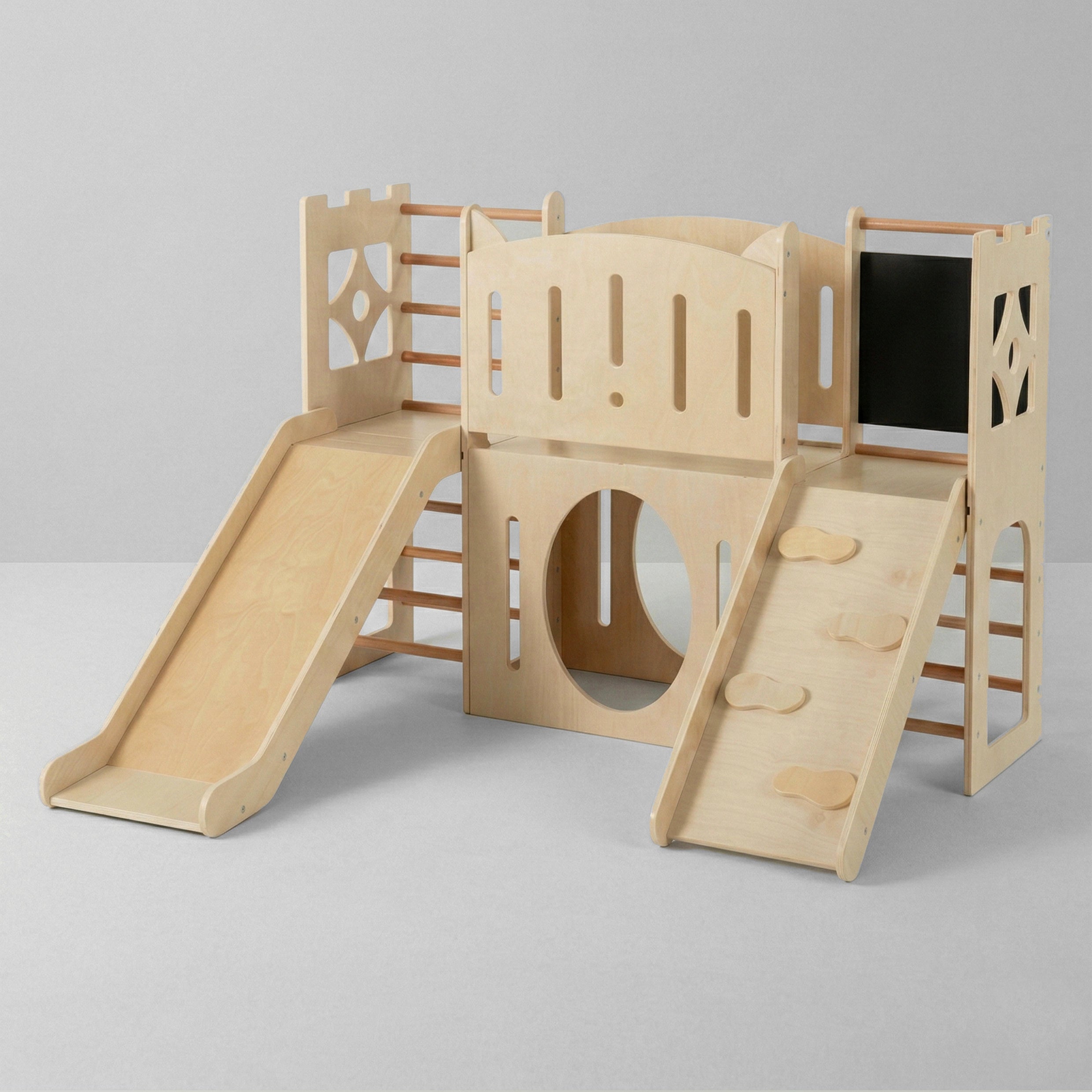 A studio shot of a light wood 8-in-1 indoor kids playground set against a clean grey background. The castle-themed playset includes a smooth slide on the left, a central crawl-through tunnel, a climbing ramp on the right, and safety rails.