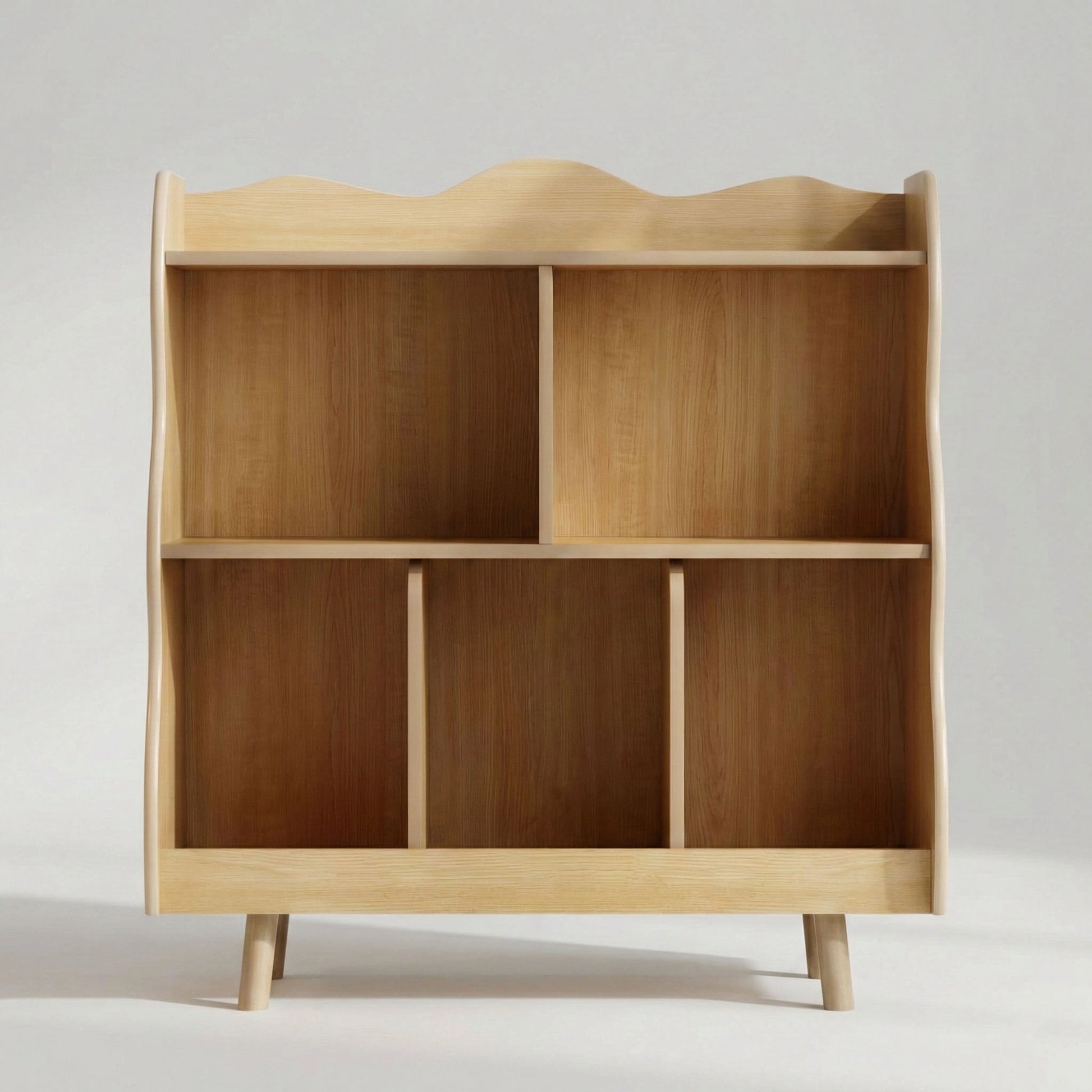 Front view of a solid wood kids bookshelf featuring a unique wavy edge design, two shelves with multiple open storage compartments, and raised legs.