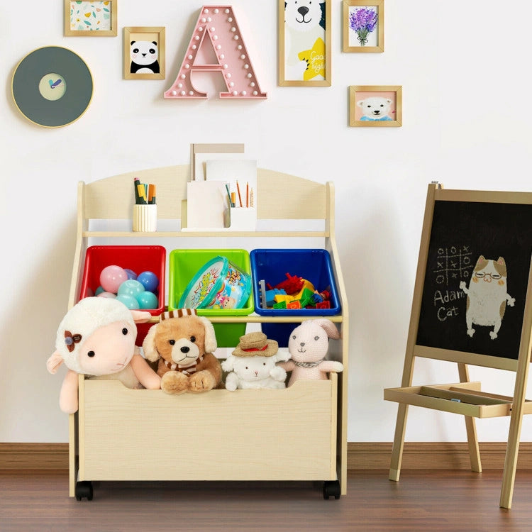 A light wood kids' toy storage organizer in a playful room setting. The unit features a top display shelf for art supplies, three removable colorful plastic bins (red, green, and blue) holding small toys, and a spacious bottom rolling wooden toy box equipped with casters, filled with plush animals.