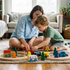 Mom accompanying toddler playing wooden train track toy on indoor floor, warm parent-child scene